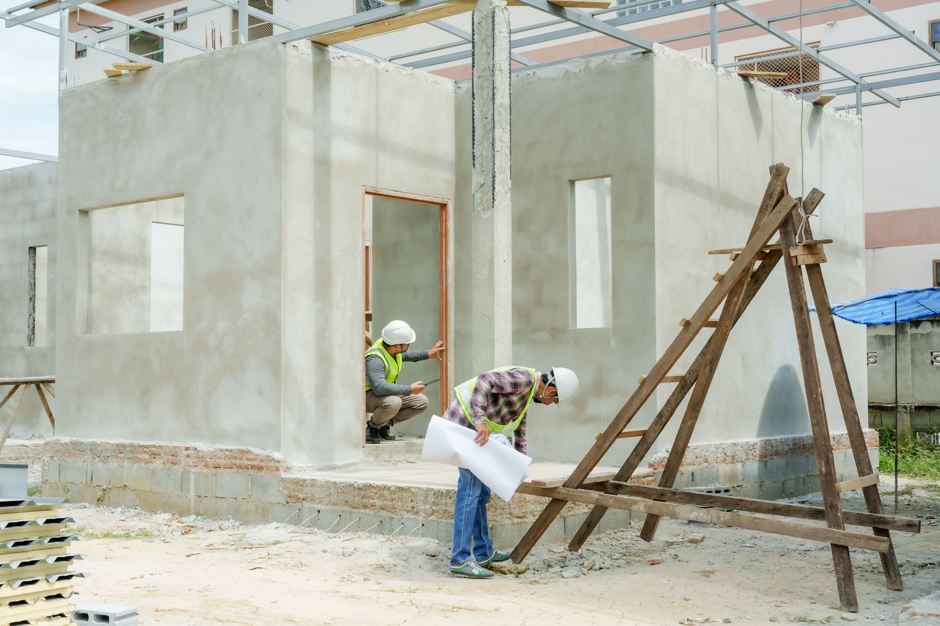 Asian architects and engineers inspecting the structure of house under construction Asian man wearing a green reflective vest and safety helmet. Standing outside. Collaboration of multiethnic people