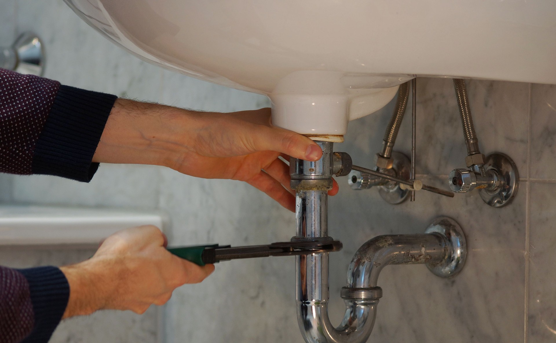 Plumbing repair service. Professional installer with spanner checking pipe.